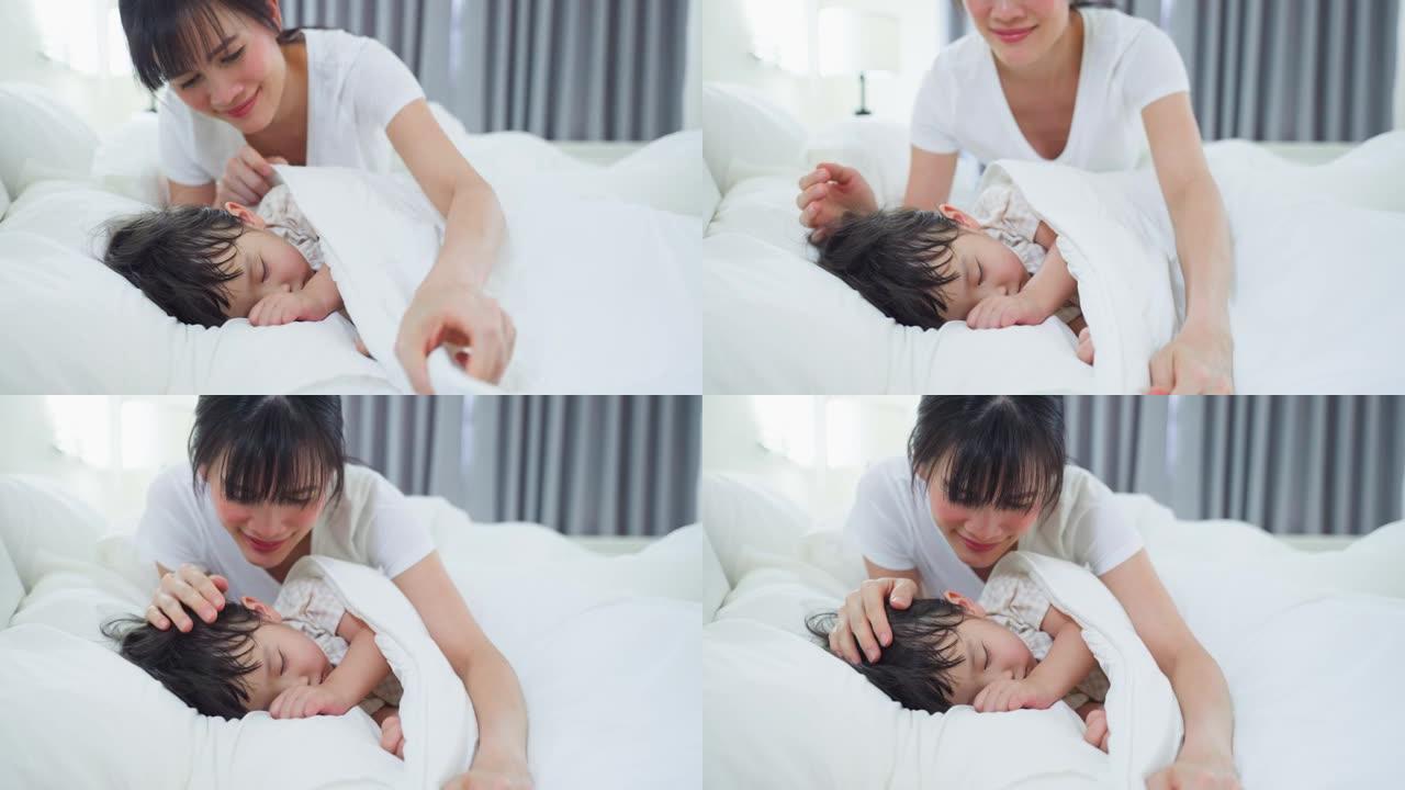 亚洲慈爱美丽的母亲照顾睡着年轻舒适的孩子。有爱心的父母妈妈早上在卧室里躺在床上睡觉的小女孩女儿上毯子