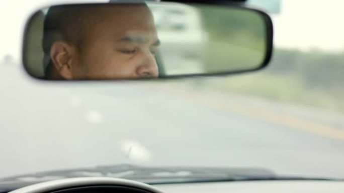 后视镜。年轻的亚洲男子司机昏昏欲睡。他打了个哈欠，正要睡着。打瞌睡，长时间开车，睡眠不足
