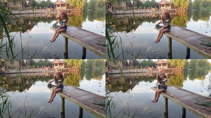 一个四岁的女孩在河上的钓鱼平台上玩耍，赤脚从水桶里倒水。