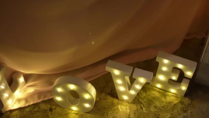婚宴上的浪漫装饰品，点燃字母拼写单词爱站在燃烧的蜡烛附近的地面上。恋爱中的人的复古照明仪式符号