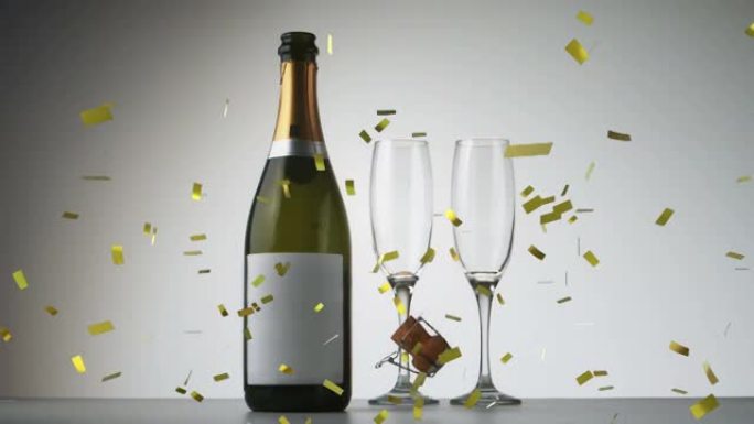 金色的五彩纸屑落在香槟瓶和灰色背景下的两个香槟杯上