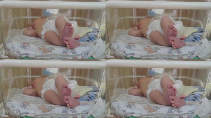 一名新生婴儿睡在产科医院病床上的透明玻璃后面，腿部特写