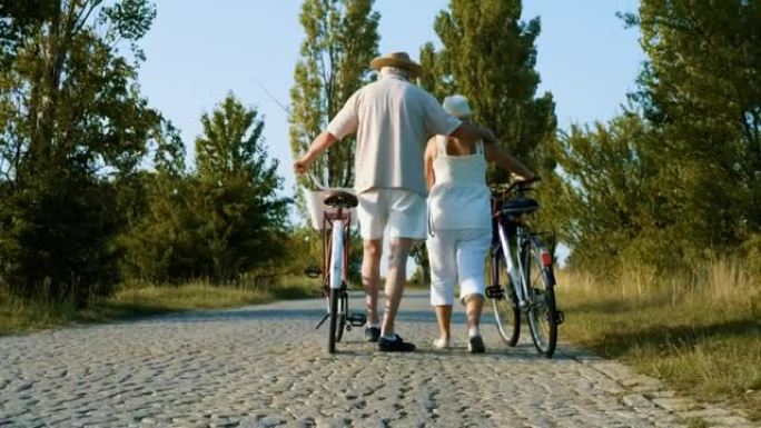从一对幸福的退休夫妇在大自然的鹅卵石路上行走和推着自行车的背后拍摄