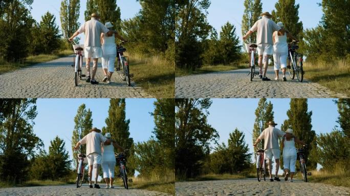 从一对幸福的退休夫妇在大自然的鹅卵石路上行走和推着自行车的背后拍摄