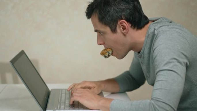 嘴里有纸杯蛋糕的人在笔记本电脑上工作