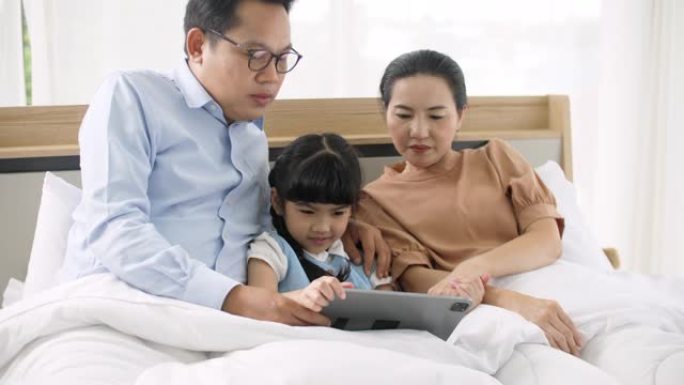 父母在床上读数字平板电脑上的电子书给女儿