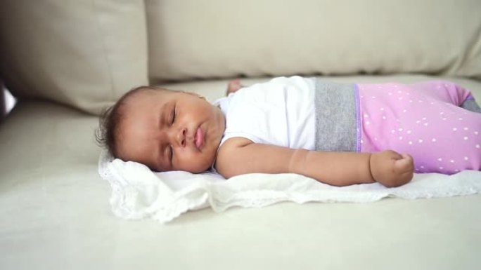 婴儿婴儿独自睡在沙发上。穿着粉色童装的混血幼儿。可爱的无辜孩子