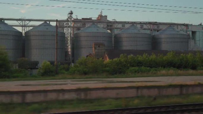 从高速火车的窗户看，在夏天背景下美丽的多云蓝天上，老生锈的棚车和钢制粮仓的景观。运输、旅行、铁路、道