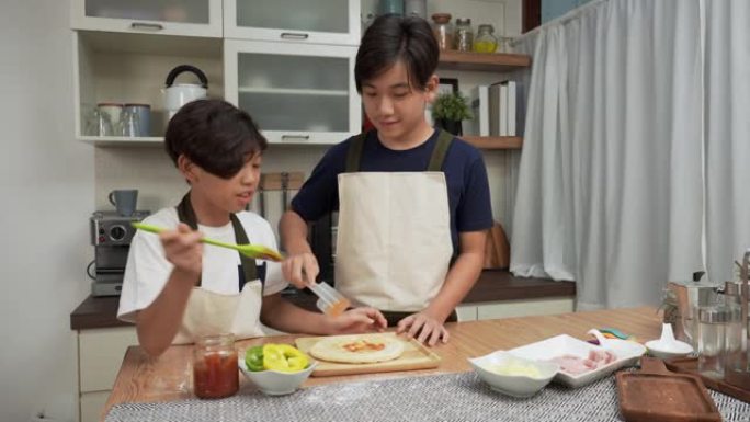 亚洲老大哥和小弟弟有一个有趣的活动，制作比萨饼，在周末添加酱汁，甜椒，火腿作为亚洲家庭的晚餐概念，有