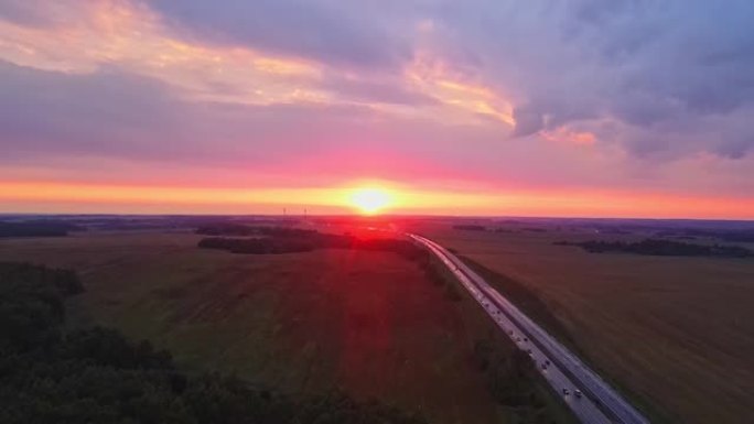 红色日落时高速公路的全景鸟瞰图。乡村田野附近有道路的景观。美丽的蜿蜒小路通向傍晚的乡村。戏剧性的天空