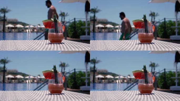 男子进入豪华度假村的游泳池，聚焦西瓜鸡尾酒杯。