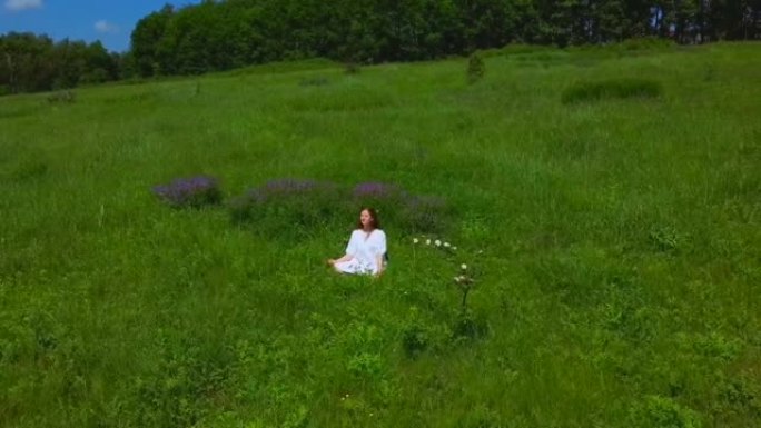 一个女人在绿野的航拍。一个年轻女孩在山上散步和采花。无人机飞越人与自然。夏天快乐。享受这一刻。