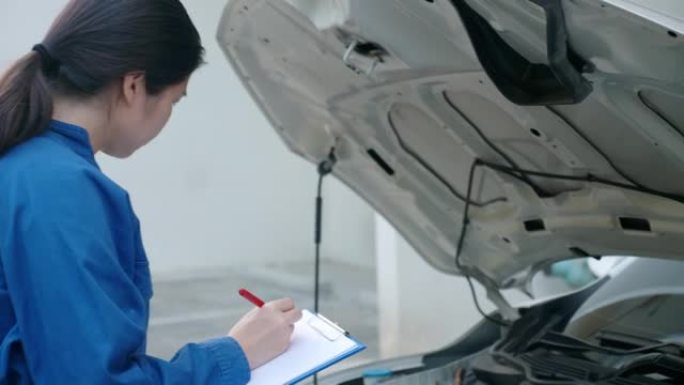 亚洲女机械师检查汽车，竖起拇指，微笑。