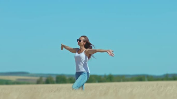 戴着墨镜的美丽女孩走过麦田，幸福的生活时刻。女孩沿着金色的田野走，双手伸向两侧，一道美丽的风景。