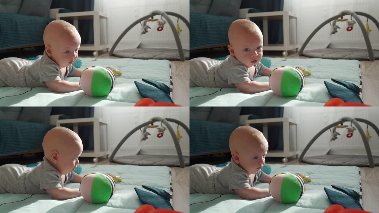 可爱的快乐宝宝玩玩具躺在肚子上的游戏垫上，三个月大男婴的脸特写。