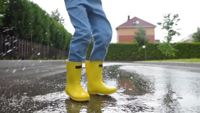 小男孩穿着黄色橡胶靴在小镇的雨天在水坑中跳跃。孩子玩得开心。