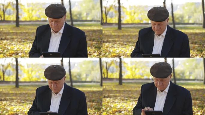 戴帽子的高级男子使用平板电脑，并在阳光明媚的秋天背景下讲述