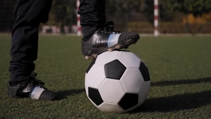 在绿色草地上的足球特写镜头，一个小男孩将脚放在球上