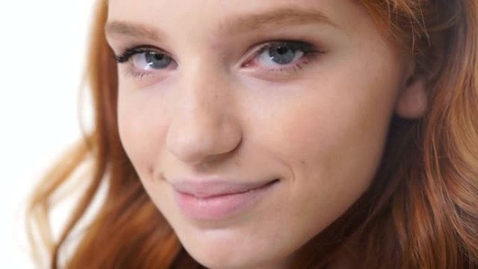 一个年轻性感的女人的特写镜头，红头发微笑着看着孤立的白色相机
