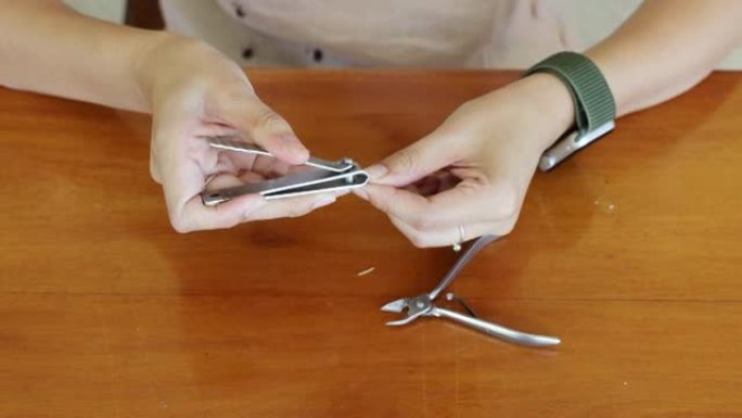 亚洲妇女在家里用指甲剪在木桌上的指甲上手工切割