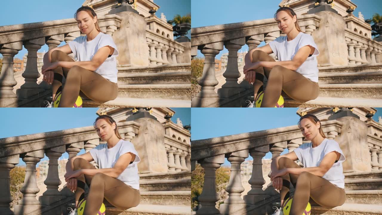 美丽的运动女孩坐在城市公园的楼梯上，梦dream以求地看着镜头