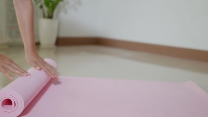 女人在运动准备工作之前或之后滚动粉红色瑜伽垫