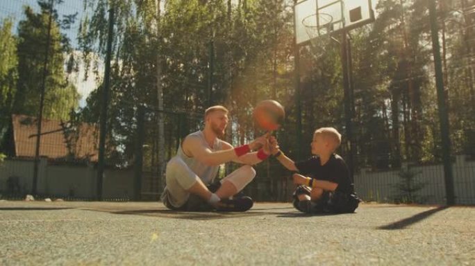运动幸福家庭。男子篮球运动员父亲在户外篮球场上学习儿子在手指上旋转球