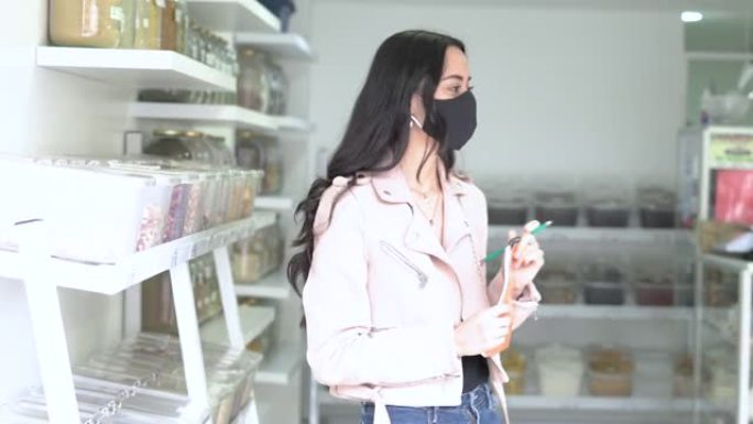 25岁的戴着口罩的拉丁妇女正在做生意，记下了缺少的食物
