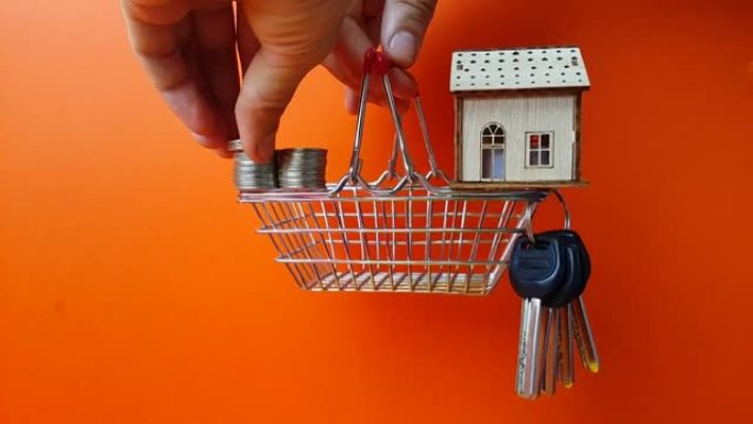买卖房地产。租一套公寓。住宅建筑的资本投资。硬币和钥匙放在超市篮子里的木屋里，人手拿着。添加硬币。