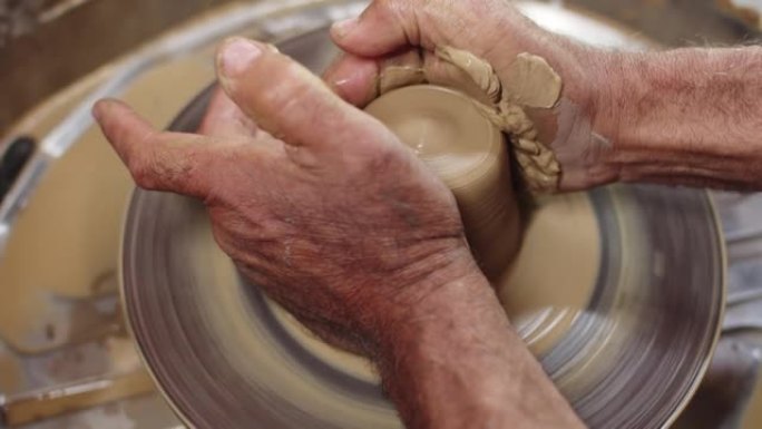 波特将粘土放在旋转的波特的轮子上，用水润湿并定型，特写。男人的手用陶工轮上的一块粘土工作，使人塑形