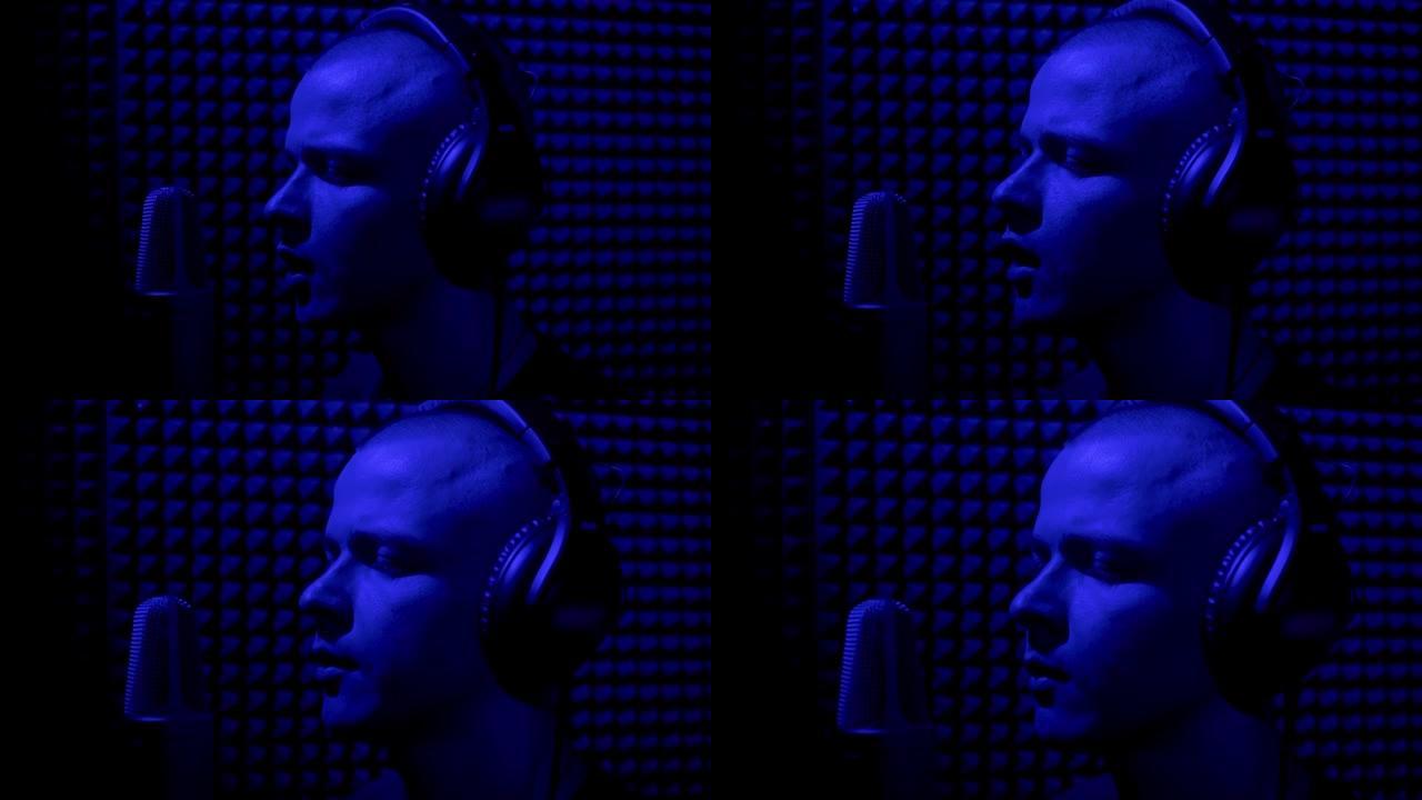男子在录音棚里用麦克风唱歌。HDR。一位年轻的男歌手在带有蓝光的音乐黑暗工作室录制歌曲的侧视图