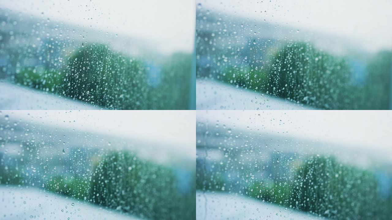 慢动作场景窗玻璃上的水滴，以模糊绿色公园背景为雨季设计理念