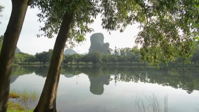 阳光照射下自然池塘的美丽早晨风景，一名穿着运动服的妇女在公园的树下锻炼并举起手臂向空中。健康的生活方