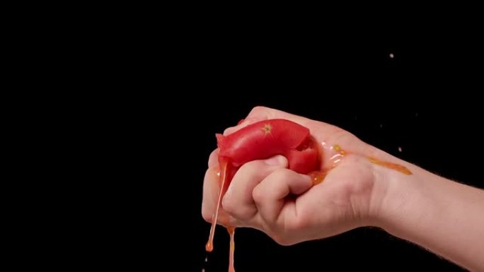 雄性手压碎新鲜的红番茄，并将健康蔬菜中的所有种子汁和果肉暴露。在工作室孤立的黑色背景上从番茄中榨汁。