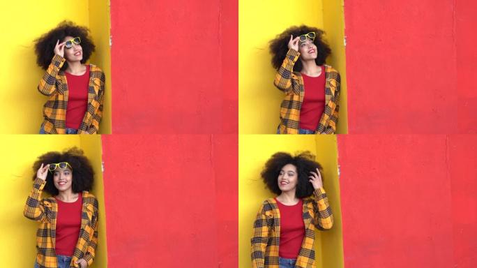 4k视频美丽的非洲裔美国女人，有着非洲的头发和五颜六色的衣服，在五颜六色的墙上微笑和姿势