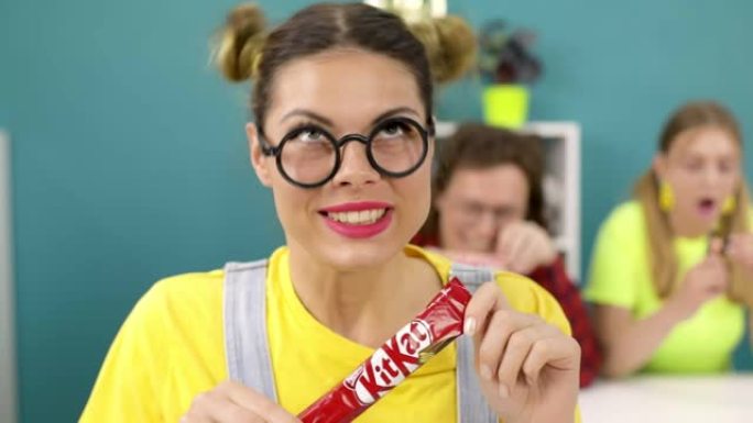 一个戴着眼镜的傻女学生在课堂上打开了一块美味的巧克力棒。
