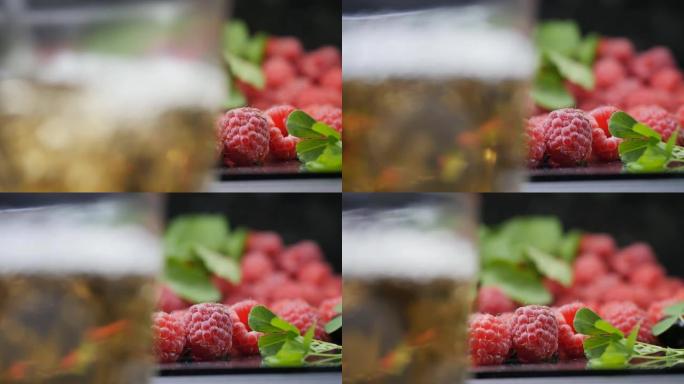 详细。将芬芳可口的浆果茶倒入玻璃杯中，背景是成熟的红树莓和绿叶。热饮。多莉镜头，特写