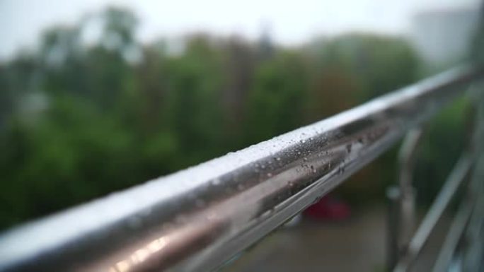 下雨了。下雨。特写。雨滴滴在阳台金属栏杆的光滑表面上，并在雨中向下流动。夏季雨天