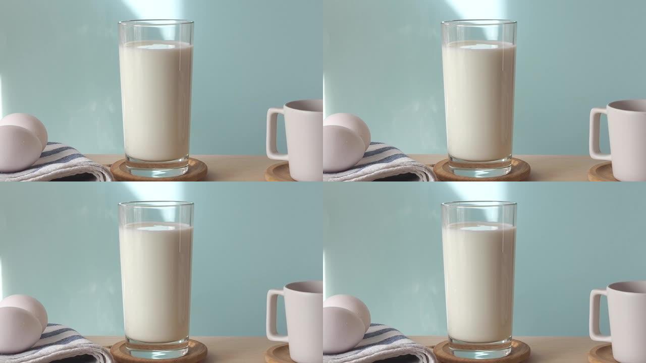 厨房桌子上有鸡蛋，杯子和一杯牛奶，在蓝墙前。牛奶视频合成。