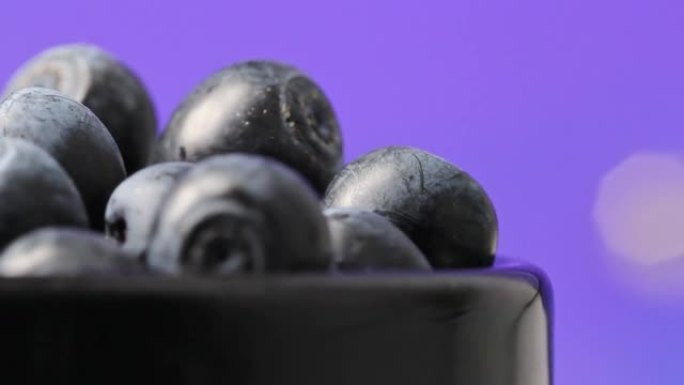 成熟的甜蓝莓浆果在黑色陶瓷杯中的深蓝色背景特写。