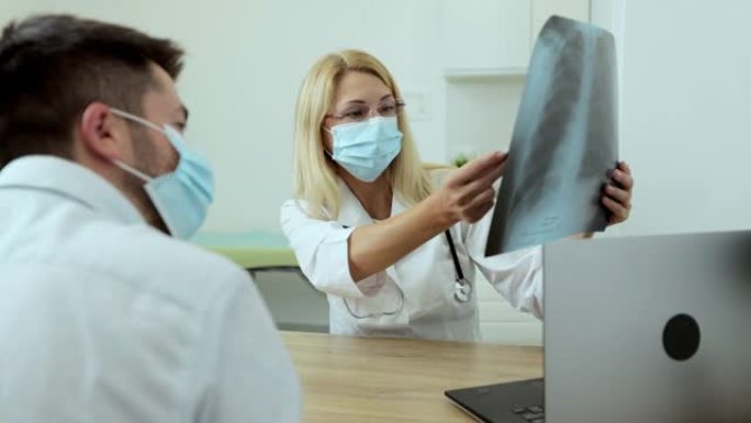 医生医生在医用口罩专家显示肺部的x射线图像，以患者解释在现代私立医院工作的症状。