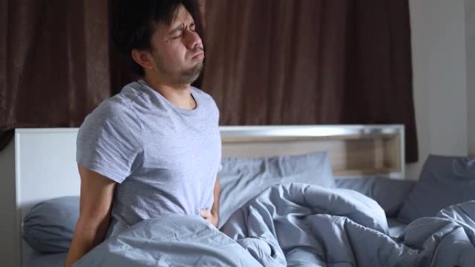 年轻的亚洲男子醒来后在床上胃痛