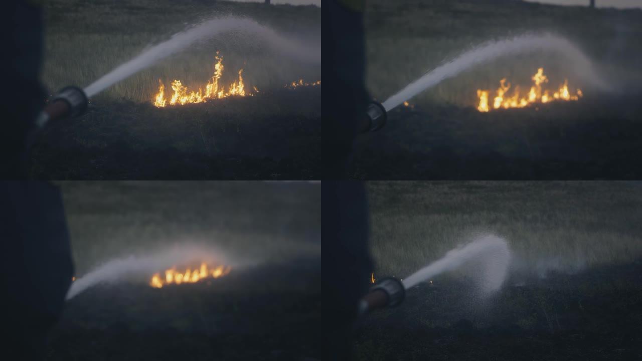 一名消防员手里拿着一根装有水的软管，扑灭了燃烧的火焰。自然物体正在燃烧: 草，草原，森林