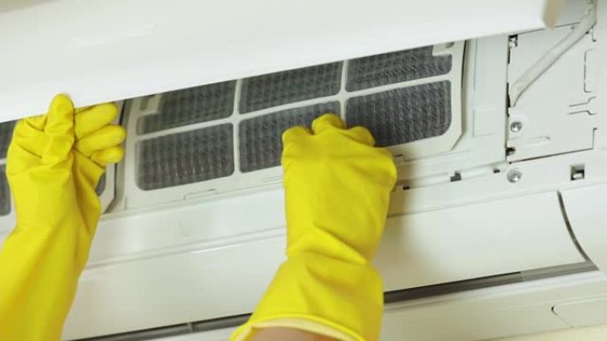 戴上黄色手套，打开空调前盖，取下过滤器进行清洁。技工服务公司的家务或工作概念