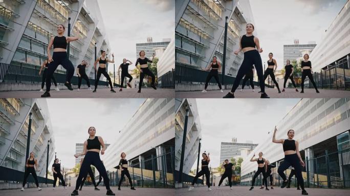 一群妇女在城市街道上表演尊巴舞，健身。穿着黑色运动服的人们在夏天的晴天在户外训练体育活动