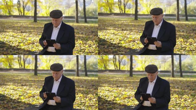 快乐的老人在公园的长椅上休息，在平板电脑上打字并告诉