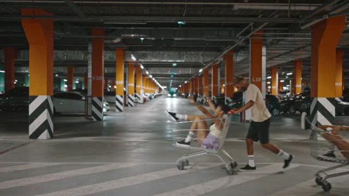 快乐的多民族朋友一起玩乐，骑在购物中心地下停车场的购物车上