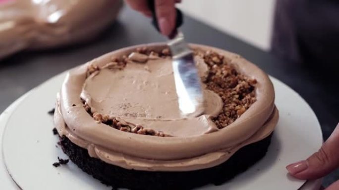4k糕点厨师将奶油榛子馅料涂在巧克力海绵蛋糕上，特写镜头。慢动作。蛋糕制作过程