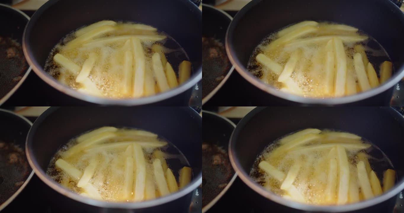 特写烹饪自制油炸黄色炸薯条土豆在厨房热沸腾飞溅油，油炸美味小吃，快餐