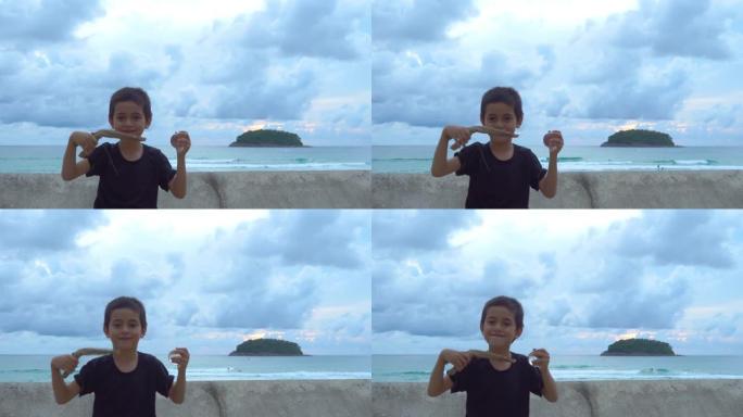 日落时分，泰国普吉岛卡塔海滩，一个男孩在海边的墙边滚动一个玻璃球。